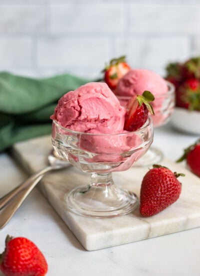 vegan strawberry frozen yogurt in a glass ice cream dish with a fresh strawberry for garnish.