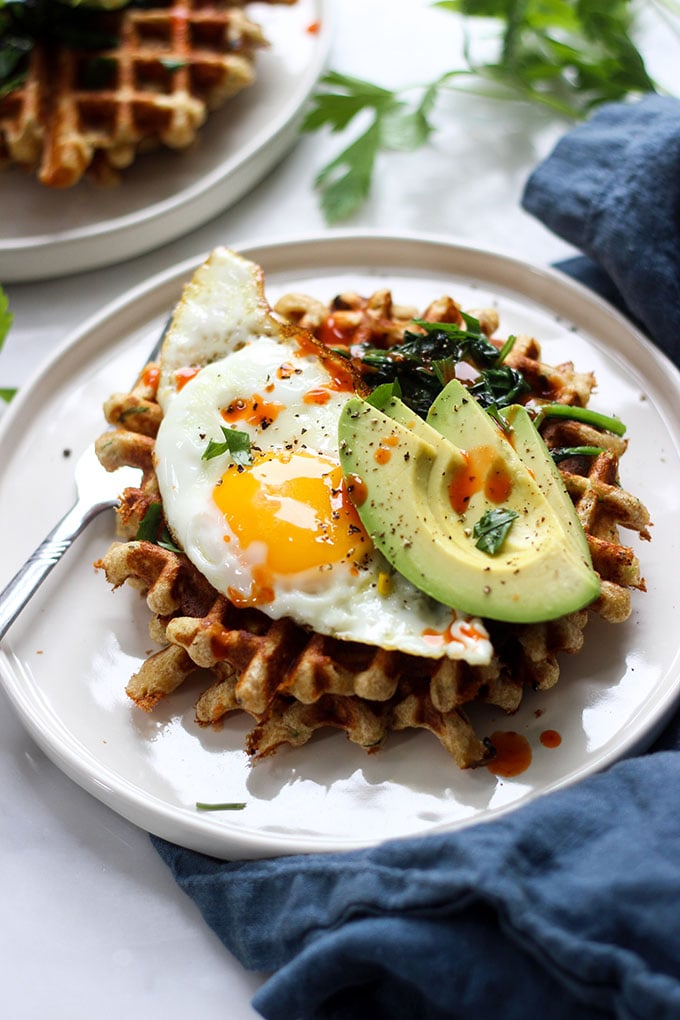 Savory Cheddar Zucchini Waffles topped with a fried egg on a white plate.