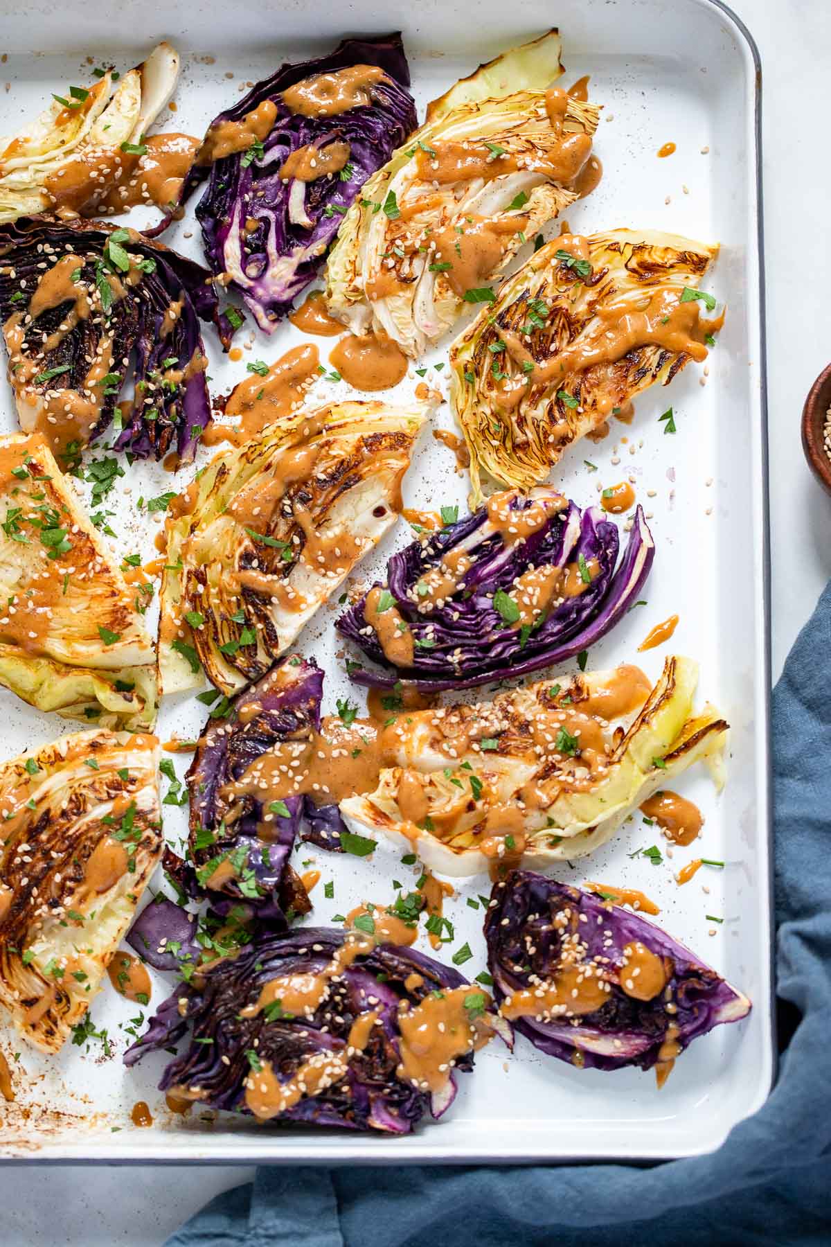 oven roasted cabbage with tahini sauce garnished with parsley and sesame seeds.
