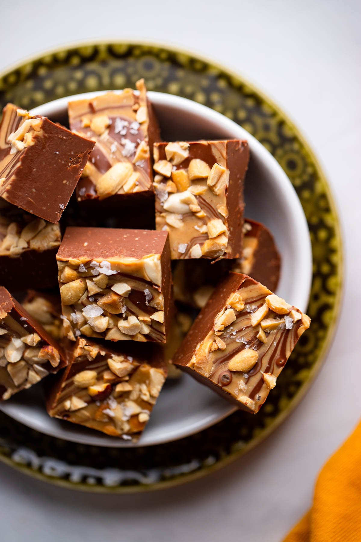 chocolate peanut butter fudge pieces garnished with flakey sea salt in a small white dish.