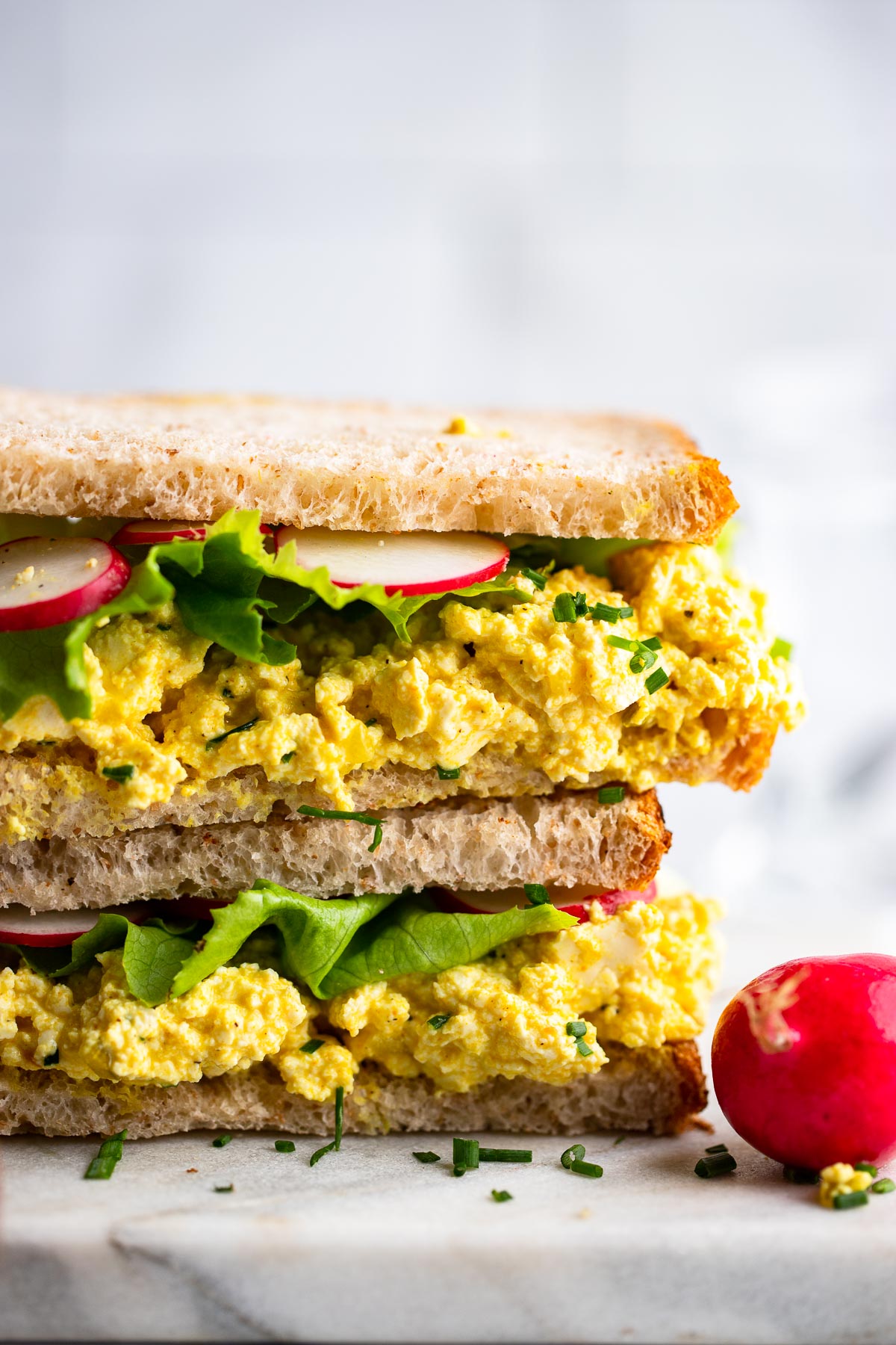 assembled tofu egg salad sandwich garnished with chives close up.