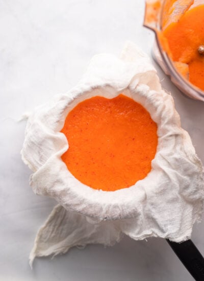 pureed carrot ginger juice ingredients added to a fine mesh strainer lined with cheesecloth.