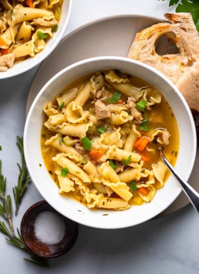 vegan chicken noodle soup in white bowl with fresh parsley as garnish.