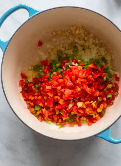 dutch oven with oil, peppers, and onions added for cooking. 