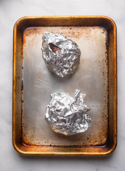 2 raw beets wrapped in aluminum foil on a metal baking sheet. 