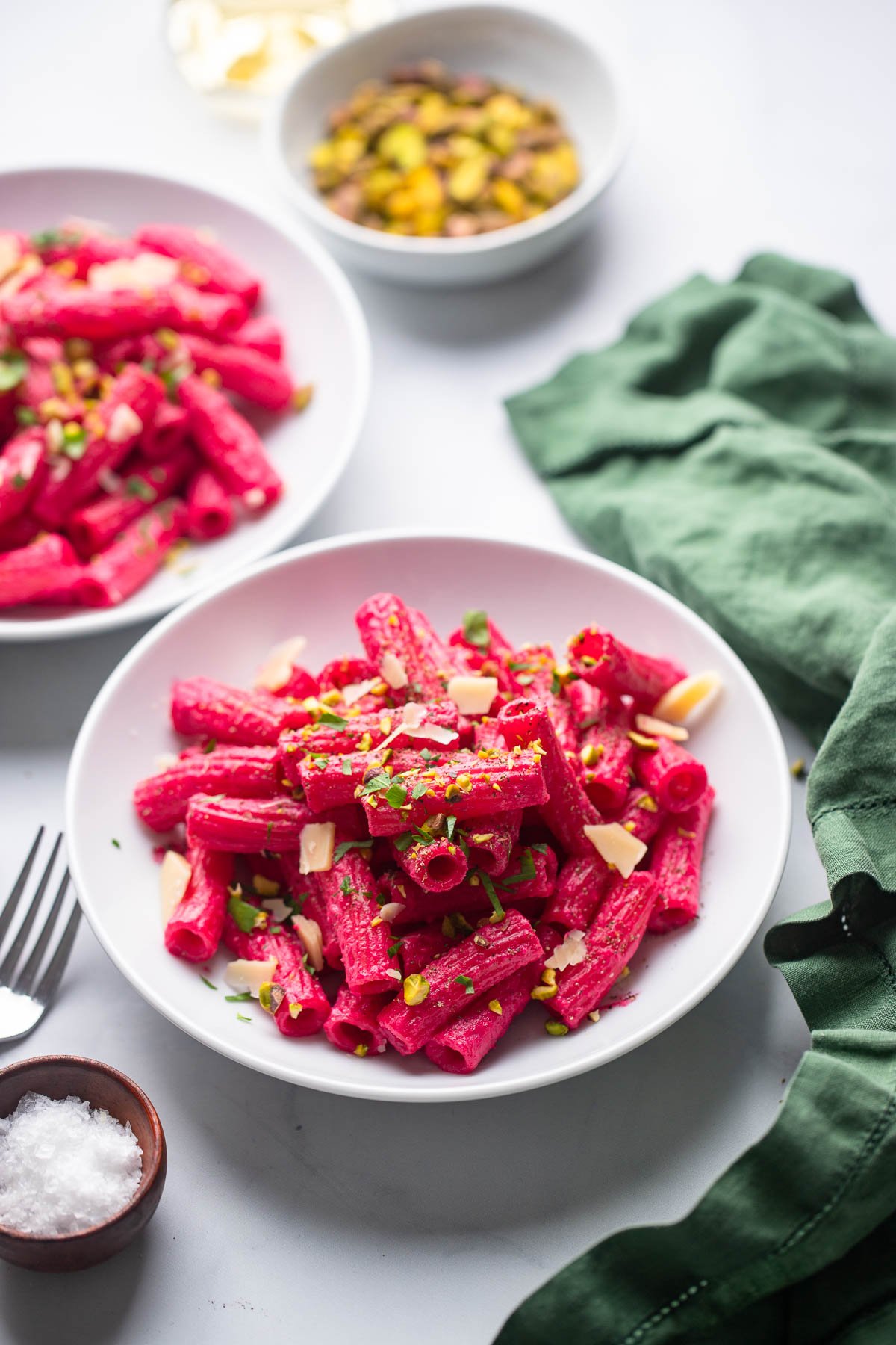 bright pink beet pasta in white bowl with chopped pistachios and parsley for garnish.