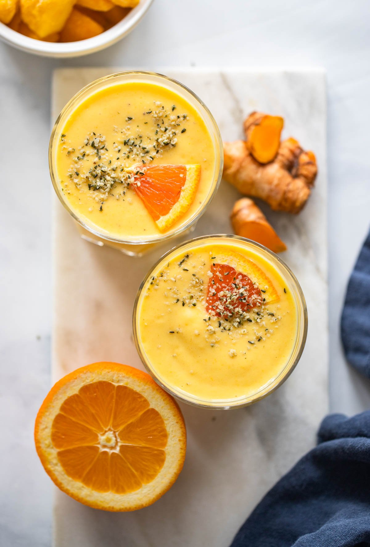 mango turmeric smoothie in 2 glasses garnished with hemp hearts and slice of orange. 