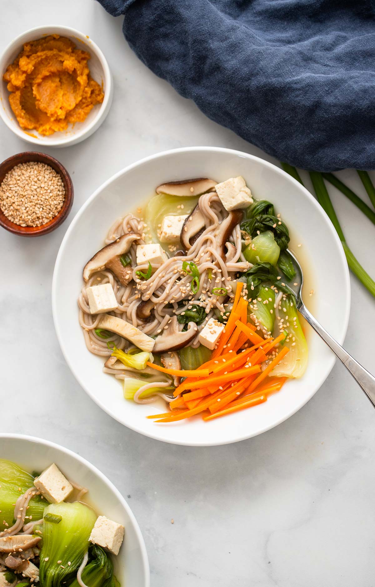 miso soba noodle soup garnished with sesame seeds in a white bowl.