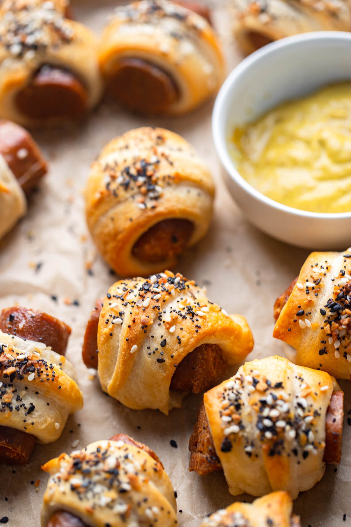 close up photo of vegan pigs in a blanket sprinkled with everything bagel seasoning on a baking sheet. 