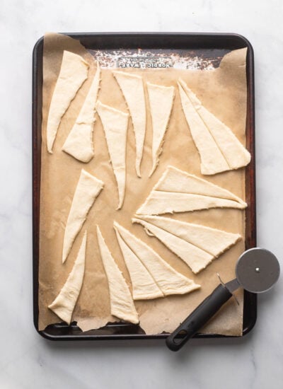 crescent roll dough separated into triangle pieces on a baking sheet with a pizza cutter. 
