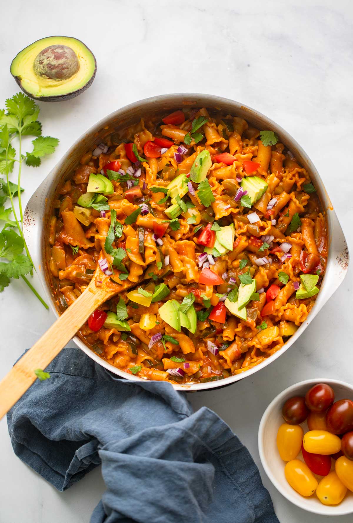 vegan taco pasta in skillet garnished with avocado, red onion, and chopped cilantro.