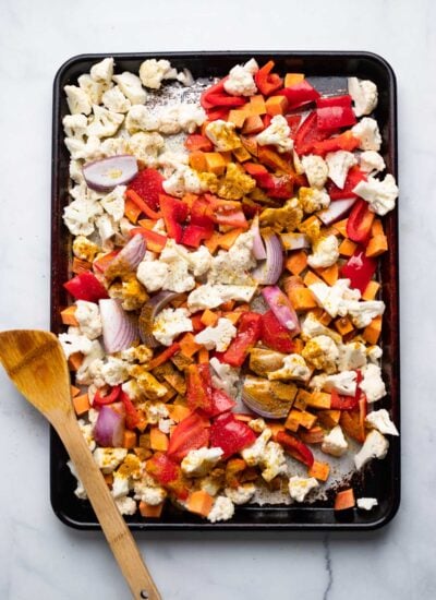 chopped vegetables spread into a single layer on a baking sheet with curry powder sprinkled on top.