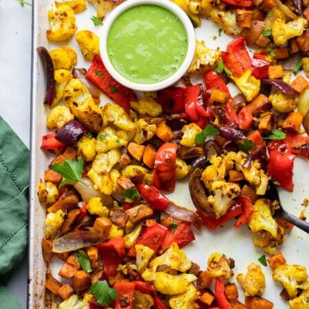curry roasted vegetables in a sheet pan with green sauce.