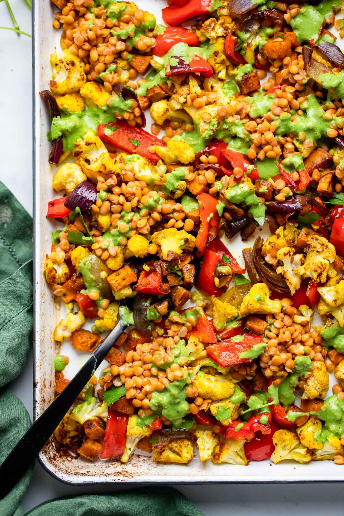 curry roasted vegetables in a sheet pan with lentils and a green sauce poured over top. 