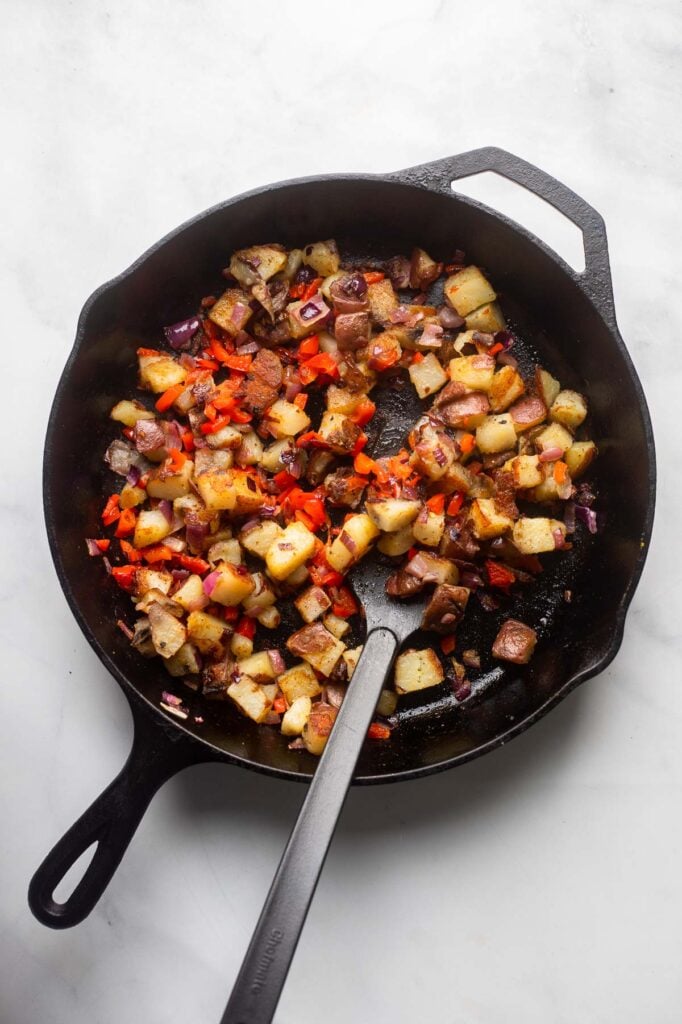 cooked breakfast potatoes in a cast iron skillet with a spatula. 