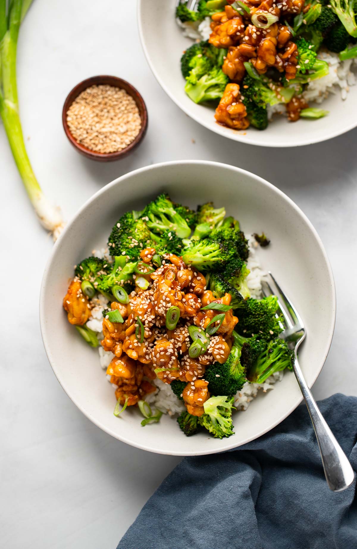 two bowls with rice, broccoli, and sticky tempeh garnished with green onion and sesame seeds. 