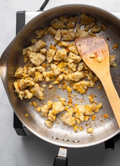 browned tempeh in a skillet with a wooden spoon. 