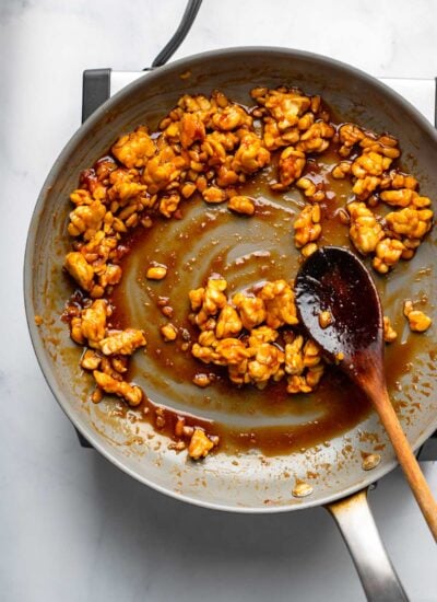 sticky tempeh in a skillet with a wooden spoon. 
