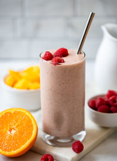 mango raspberry smoothie in a tall glass with a metal straw.