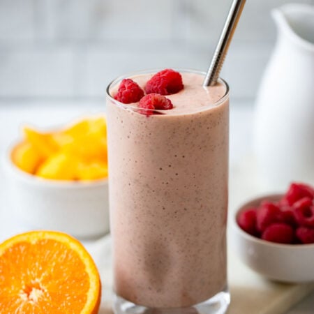 mango raspberry smoothie in a tall glass with a metal straw.