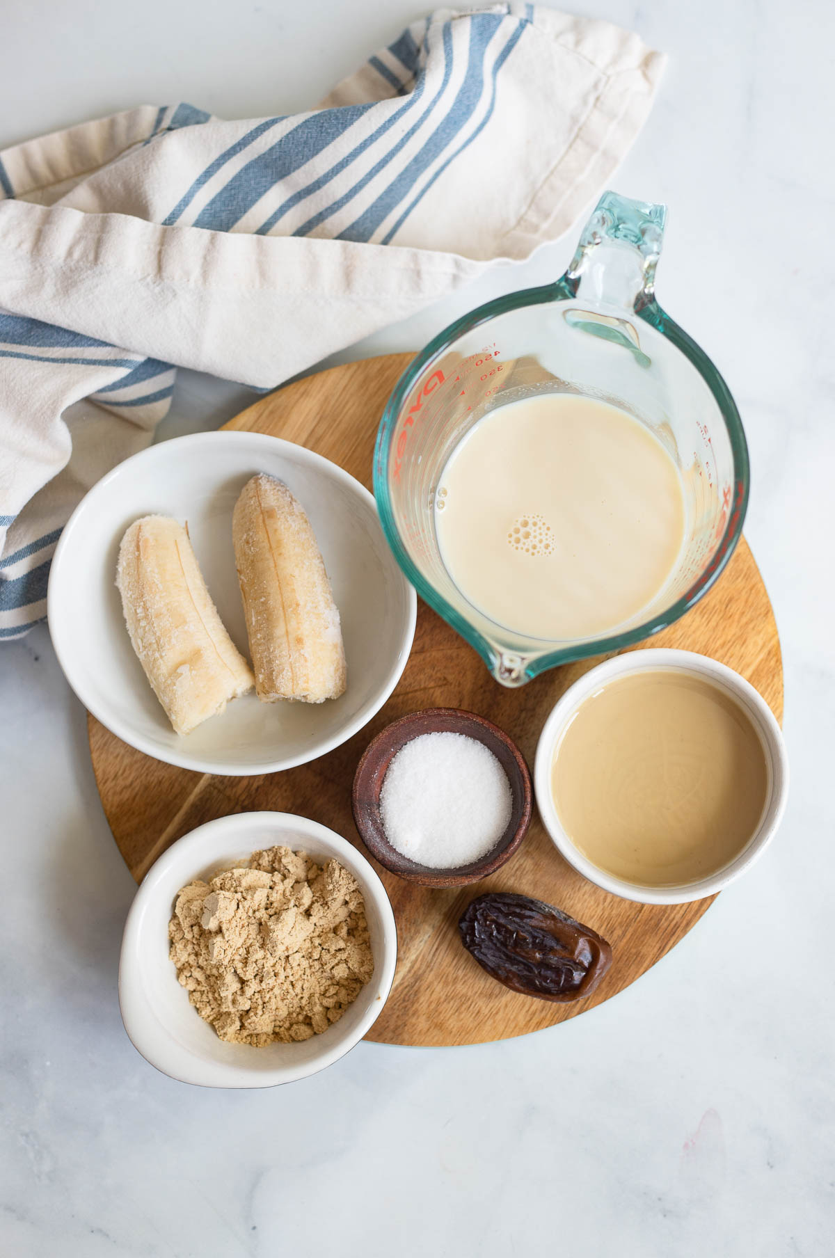 tahini smoothie ingredients in small white bowls on a ground cutting board. 