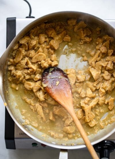 vegan plant based chicken in a skillet cooking with green enchilada sauce.
