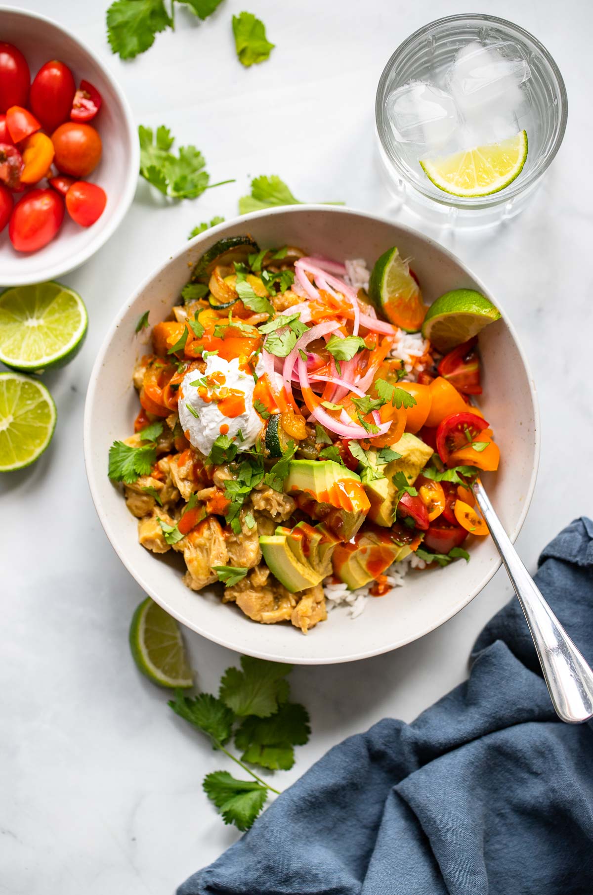 assembled vegan tex mex bowl garnished with cilantro, vegan sour cream, and pickled red onion on a white background.