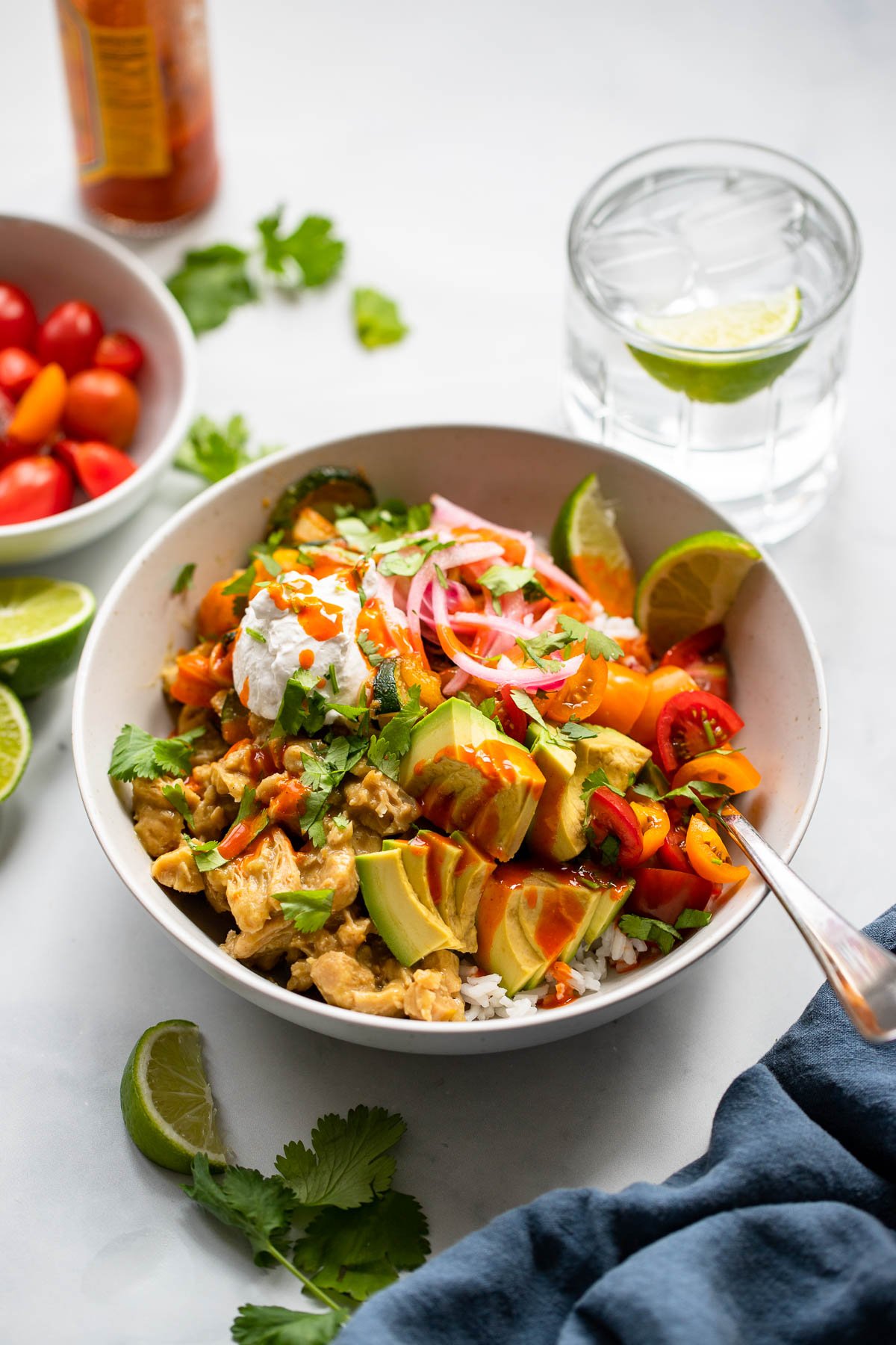 assembled vegan tex mex bowl garnished with cilantro, vegan sour cream, and pickled red onion on a white background.