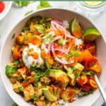 assembled tex mex bowl topped with sour cream, cilantro, and fresh tomatoes.