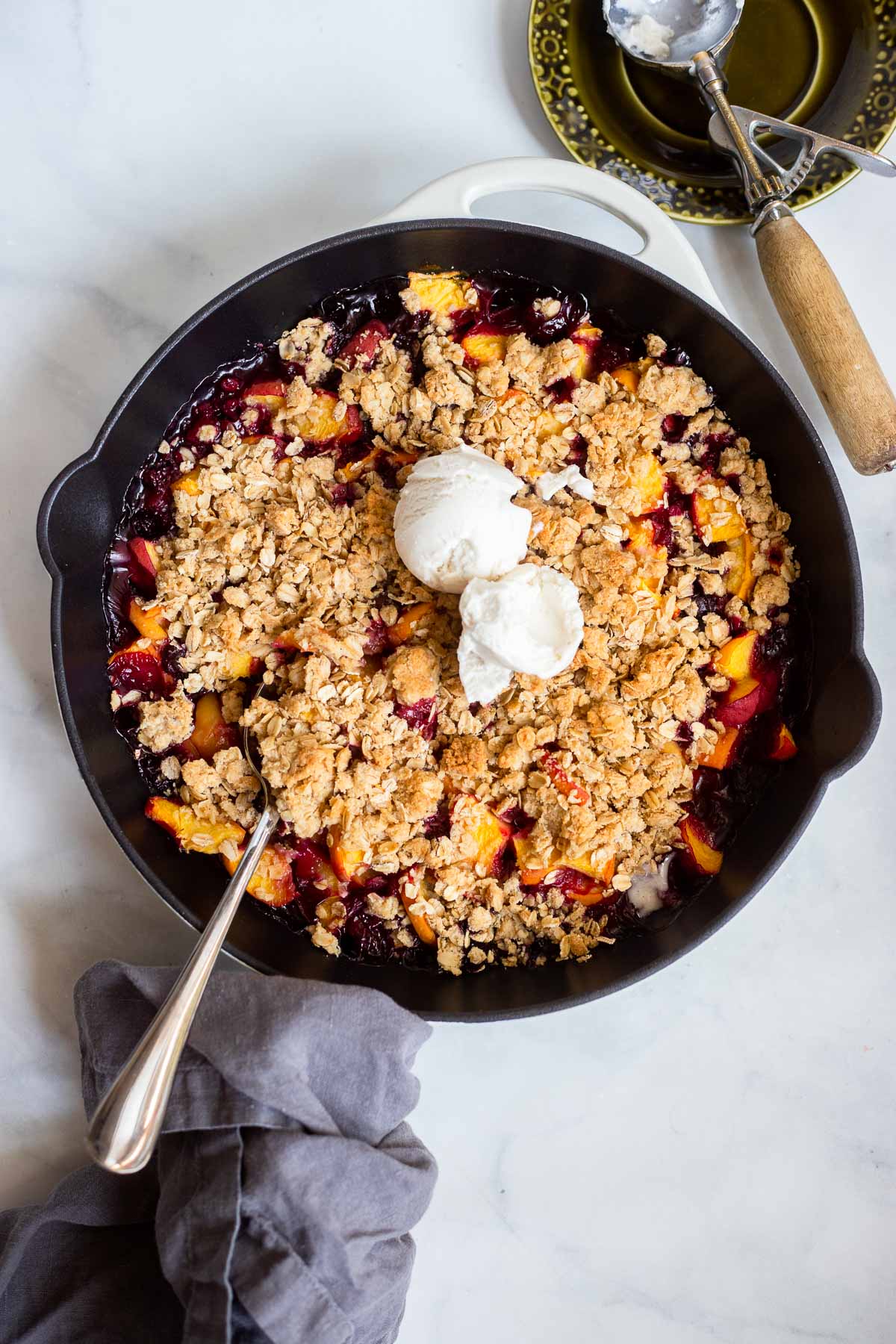peach blueberry crisp in a skillet topped with 2 scoops of ice cream. 