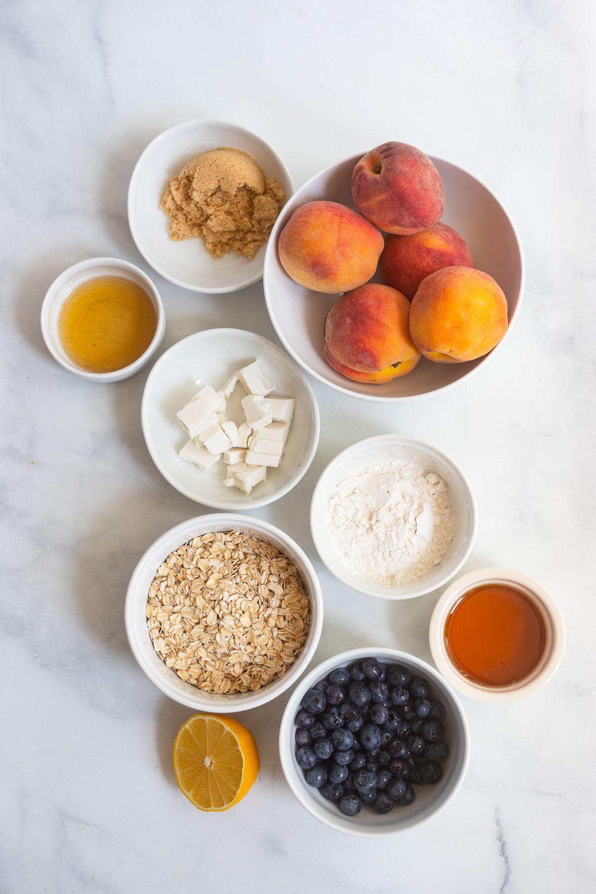 peach blueberry crisp ingredients in small bowls on a white background. 