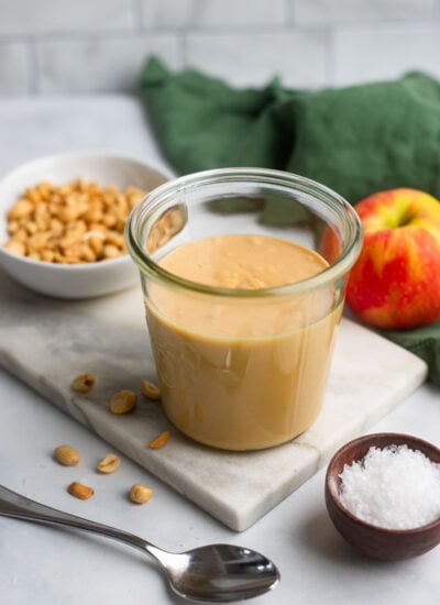 homemade peanut butter in a glass jar next to an apple.