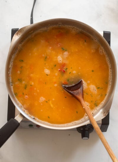 risotto ingredients cooking in a skillet with a wooden spoon. 