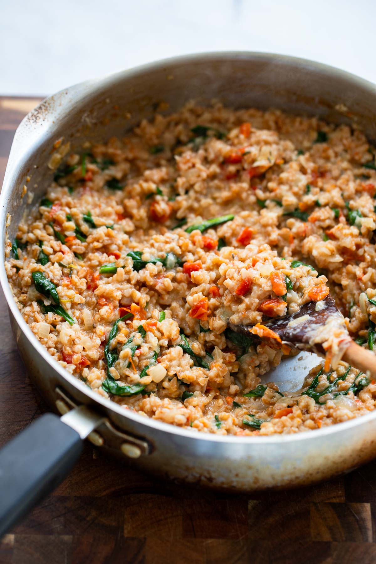 cooked farro risotto in a skillet with a wooden spoon. 