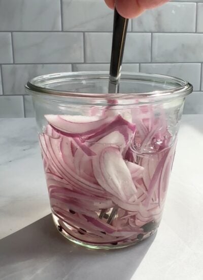 sliced red onions in a jar with pickling liquid being stirred with a fork. 