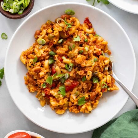 vegan chili mac in a white bowl garnished with green onions.
