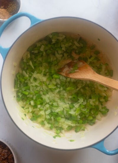 cooked diced onion and bell pepper in a dutch oven with a wooden spoon. 