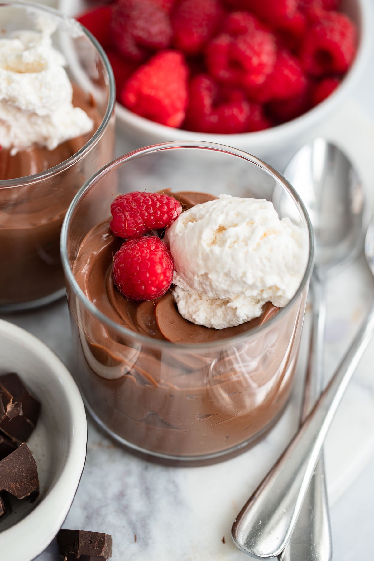 chocolate tofu mousse in a glass topped with whipped cream and fresh raspberries.