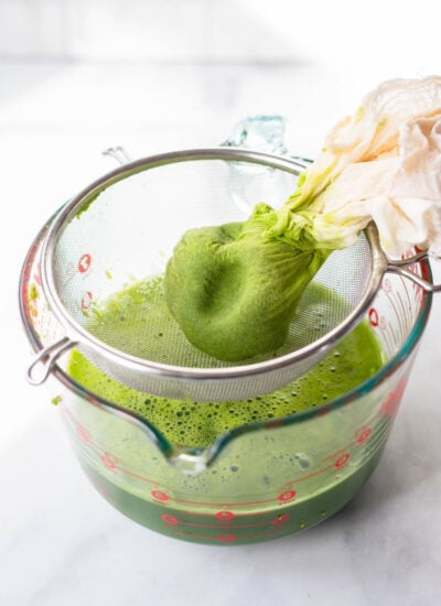 green juice squeezed out of a cheesecloth over a strainer. 