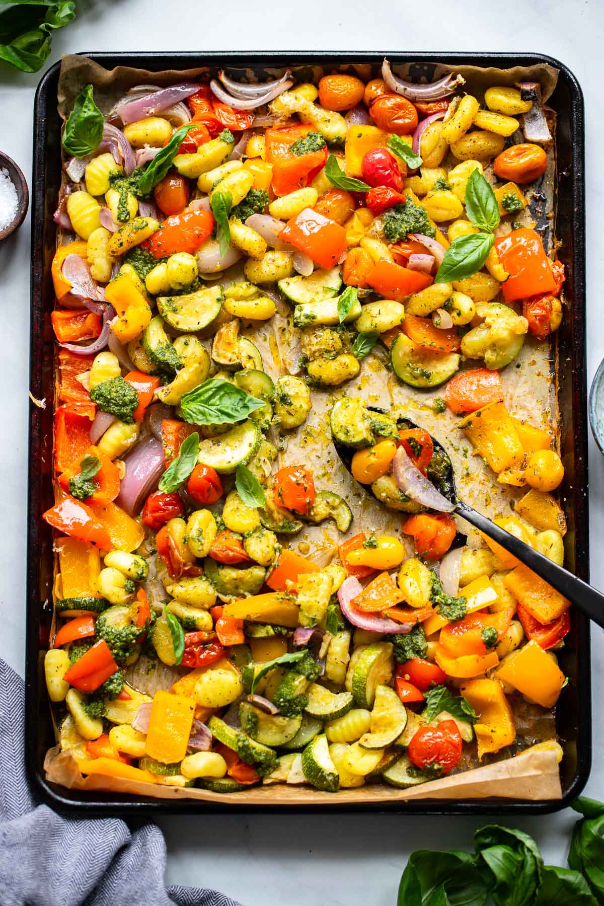 sheet pan gnocchi tossed with pesto on with a serving spoon.