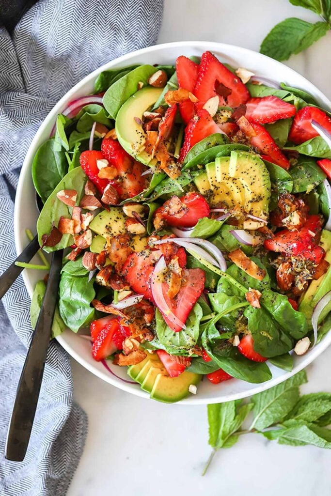 spinach and strawberry salad in a white bowl with a serving spoon.