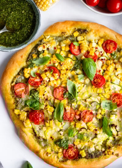 uncut sweet corn pizza garnished with fresh basil leaves on a white background.